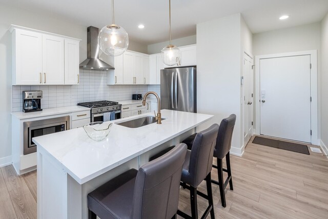 917 Harbor Dr E, Saint Joseph, MI 49085 - kitchen with appliances with stainless steel finishes, wall chimney exhaust hood, a sink, a breakfast bar, and light wood-style floors
