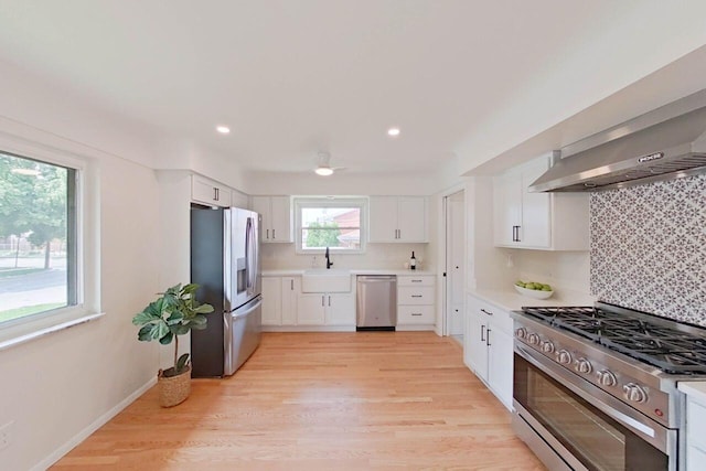 2113 12th St, Wyandotte, MI 48192 - kitchen featuring stainless steel appliances, a sink, white cabinetry, light wood-style floors, and wall chimney exhaust hood