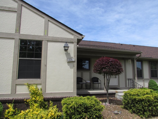 9920 Camridge Ct, South Lyon, MI 48178 - doorway to property featuring covered porch, stucco siding, and a shingled roof