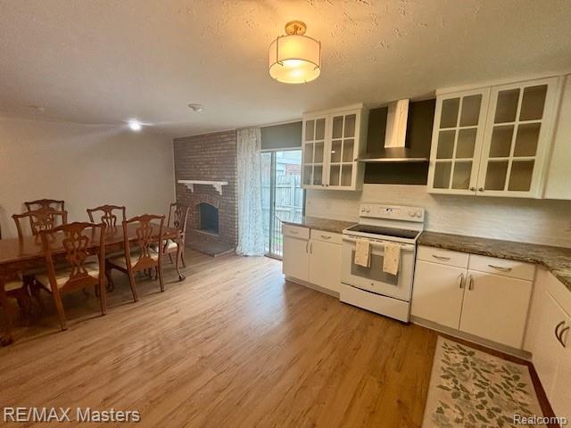 43242 Barchester Rd, Canton, MI 48187 - kitchen with white electric range oven, wall chimney exhaust hood, light wood finished floors, a brick fireplace, and white cabinetry