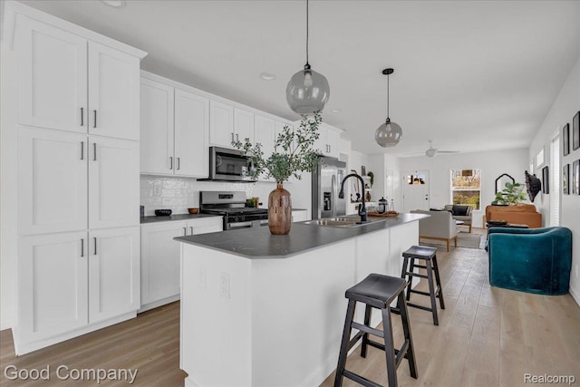 2819 16th St, Detroit, MI 48216 - kitchen featuring appliances with stainless steel finishes, a kitchen island with sink, light wood finished floors, a breakfast bar area, and white cabinets