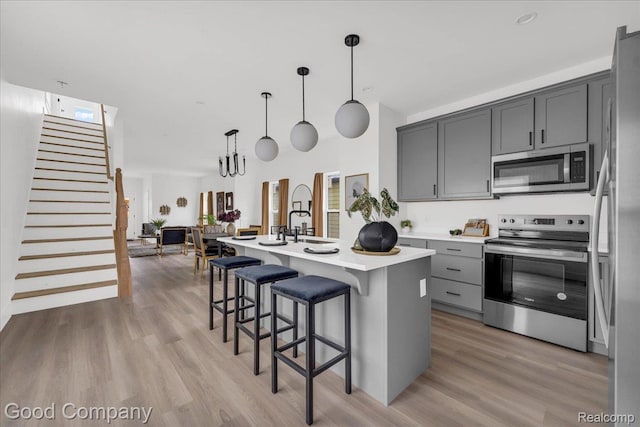 2827 16th St, Detroit, MI 48216 - kitchen featuring stainless steel appliances, light countertops, light wood finished floors, a center island with sink, and a kitchen breakfast bar