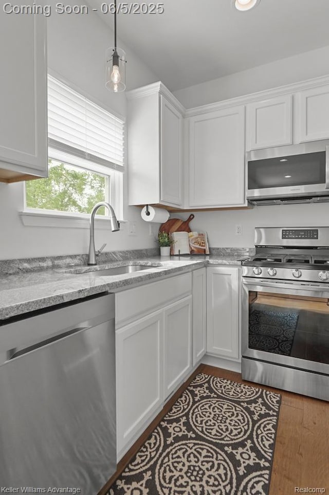 861 N Mill St, South Lyon, MI 48178 - kitchen with appliances with stainless steel finishes, a sink, white cabinetry, wood finished floors, and decorative light fixtures
