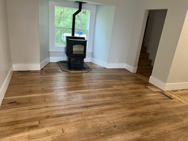 855 E Hansen Rd, Scottville, MI 49454 - unfurnished living room featuring a wood stove, hardwood / wood-style flooring, baseboards, and stairway