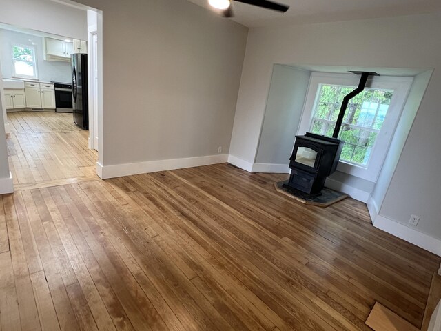855 E Hansen Rd, Scottville, MI 49454 - unfurnished living room featuring a wood stove, wood-type flooring, ceiling fan, and baseboards
