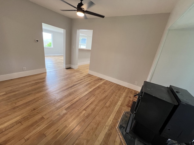 855 E Hansen Rd, Scottville, MI 49454 - unfurnished living room featuring a wood stove, light wood finished floors, a ceiling fan, and baseboards