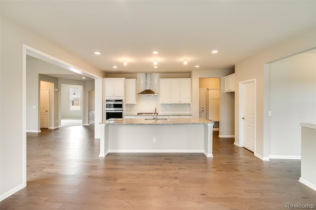 3660 Hayes Ct, Ypsilanti, MI 48197 - kitchen featuring wall chimney range hood, double oven, recessed lighting, white cabinetry, and an island with sink