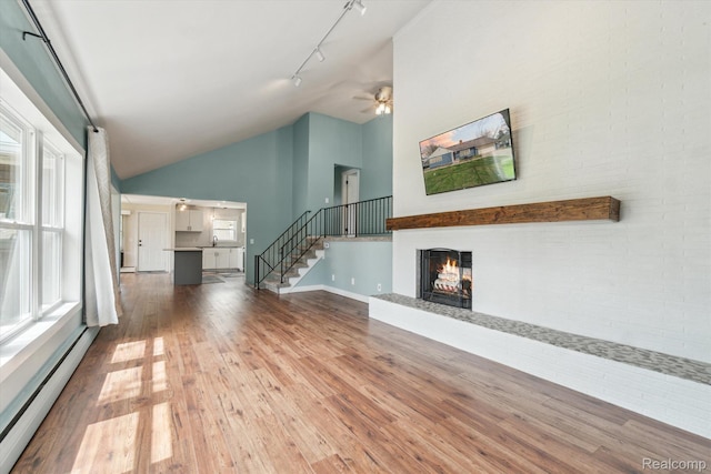 2064 N Long Lake Rd, Fenton, MI 48430 - unfurnished living room featuring a baseboard radiator, track lighting, a lit fireplace, hardwood / wood-style floors, and ceiling fan