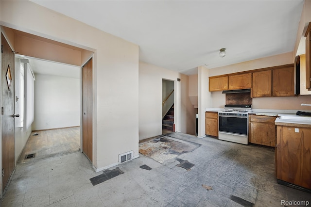 13332 Masonic Blvd, Warren, MI 48088 - kitchen with white range with gas cooktop, light countertops, brown cabinets, a sink, and under cabinet range hood
