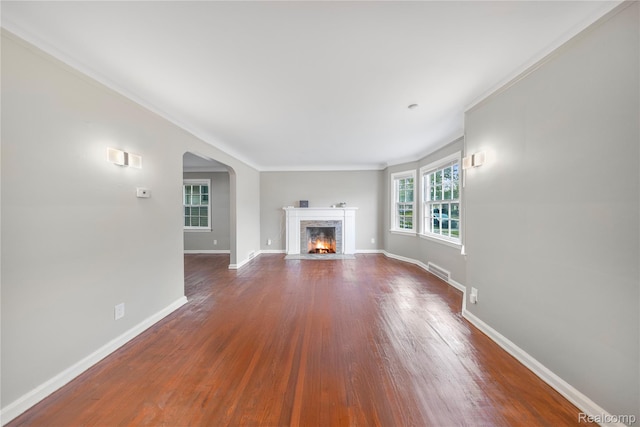 3951 Devonshire Rd, Detroit, MI 48224 - unfurnished living room featuring arched walkways, baseboards, dark wood-type flooring, ornamental molding, and a premium fireplace