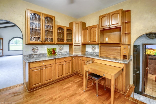5379 N Irish Rd, Davison, MI 48423 - kitchen with arched walkways, glass insert cabinets, stone countertops, light wood-style floors, and brown cabinetry