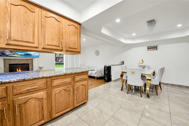 37288 Vernon Dr, Sterling Heights, MI 48310 - kitchen featuring light stone counters, a tray ceiling, light tile patterned floors, a lit fireplace, and baseboards