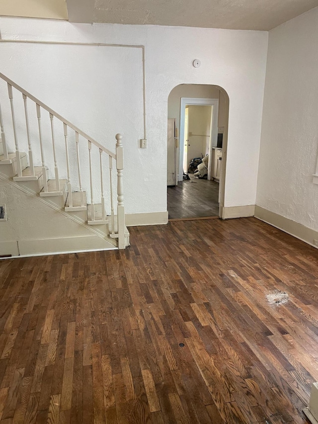 1122 Prospect St, Lansing, MI 48912 - unfurnished room with dark wood-style flooring, arched walkways, stairway, baseboards, and a textured wall