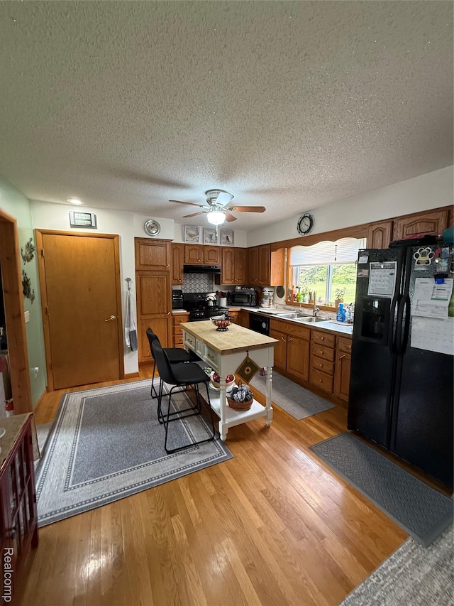 3454 Pine St, Hale, MI 48739 - kitchen with black appliances, a sink, light wood-style flooring, a textured ceiling, and light countertops