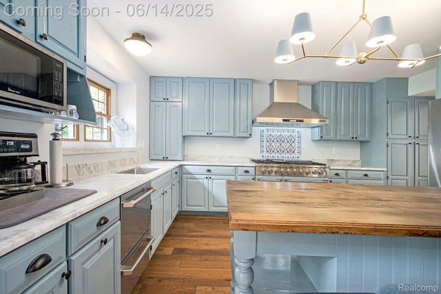 9818 Burning Tree Dr, Grand Blanc, MI 48439 - kitchen featuring wall chimney range hood, wood counters, appliances with stainless steel finishes, dark wood-style floors, and a chandelier