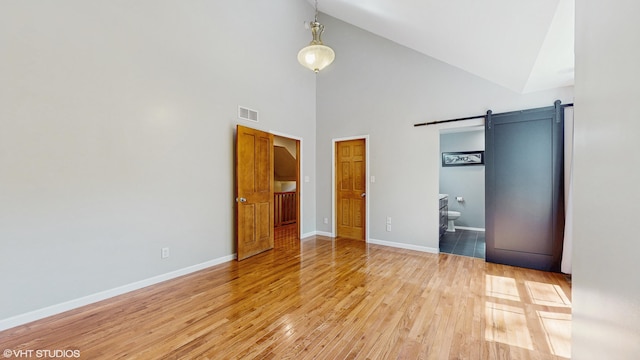 224 S Jameson St, New Buffalo, MI 49117 - unfurnished bedroom with a barn door, high vaulted ceiling, light wood finished floors, baseboards, and ensuite bath