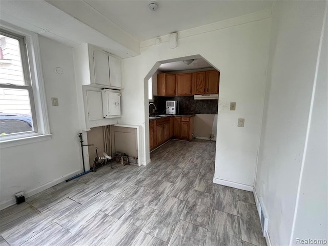 21731 Nevada Ave, Eastpointe, MI 48021 - kitchen featuring arched walkways, brown cabinets, under cabinet range hood, tasteful backsplash, and light wood-style floors