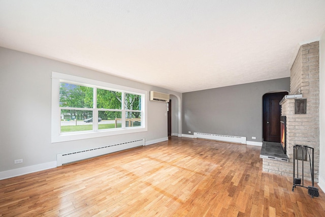 455 N 10th St, Plainwell, MI 49080 - unfurnished living room featuring a baseboard radiator, arched walkways, an AC wall unit, and light wood-type flooring