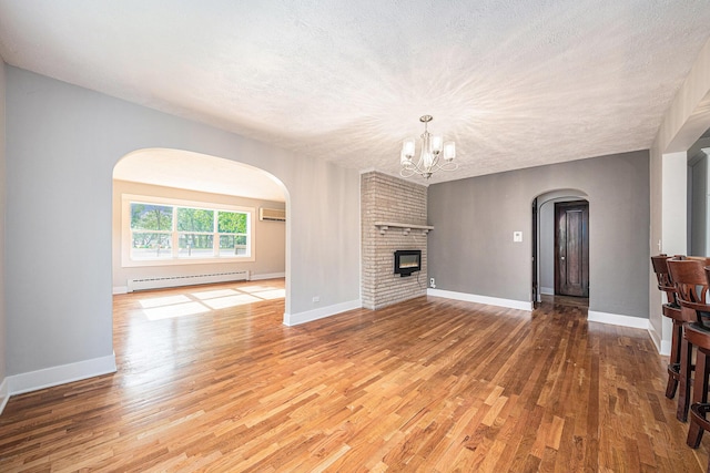 455 N 10th St, Plainwell, MI 49080 - unfurnished living room featuring arched walkways, baseboard heating, wood finished floors, a wall mounted AC, and a chandelier
