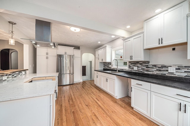 455 N 10th St, Plainwell, MI 49080 - kitchen featuring freestanding refrigerator, arched walkways, a sink, decorative backsplash, and light wood-style flooring