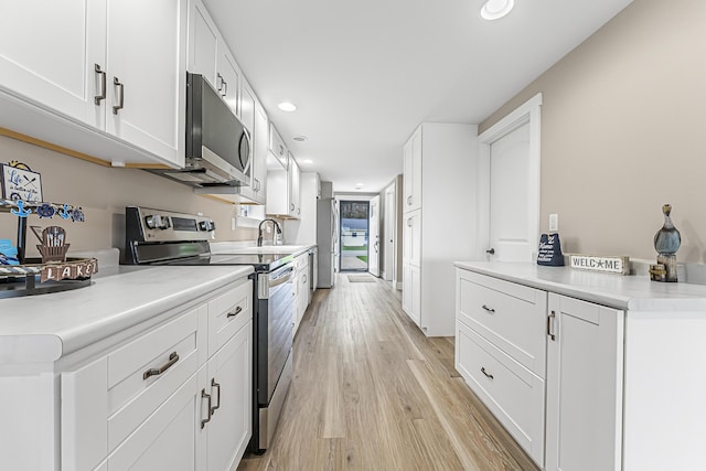 3551 W W Lake Mitchell Dr, Cadillac, MI 49601 - kitchen with appliances with stainless steel finishes, recessed lighting, white cabinets, light wood-style flooring, and light countertops