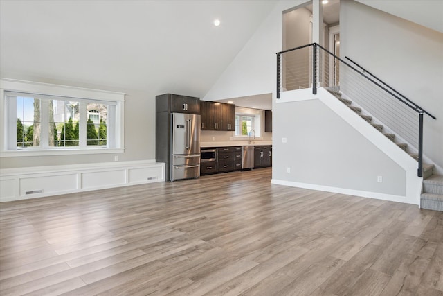 5150 Redding Dr, Pinckney, MI 48169 - unfurnished living room with high vaulted ceiling, a sink, light wood-style floors, stairway, and recessed lighting