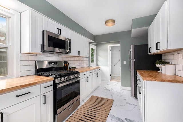 1700 Bristol Ave NW, Grand Rapids, MI 49504 - kitchen with appliances with stainless steel finishes, butcher block countertops, light marble finish flooring, white cabinets, and backsplash