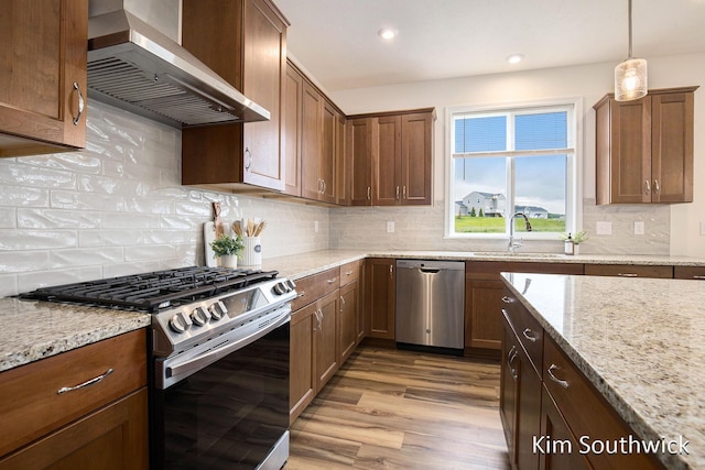 12285 Apple Cart Ln, Lowell, MI 49331 - kitchen featuring appliances with stainless steel finishes, wall chimney range hood, wood finished floors, a sink, and light stone counters