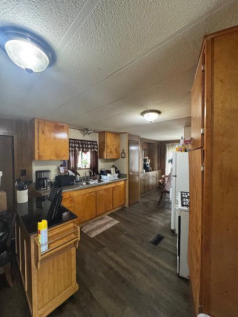 583 S Mcintosh Ln, Muskegon, MI 49442 - kitchen with brown cabinets, dark wood-style floors, a sink, a textured ceiling, and a peninsula