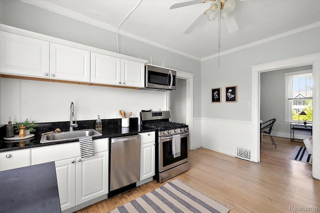 2160 Concord St, Detroit, MI 48207 - kitchen with stainless steel appliances, light wood-type flooring, white cabinets, ornamental molding, and a ceiling fan