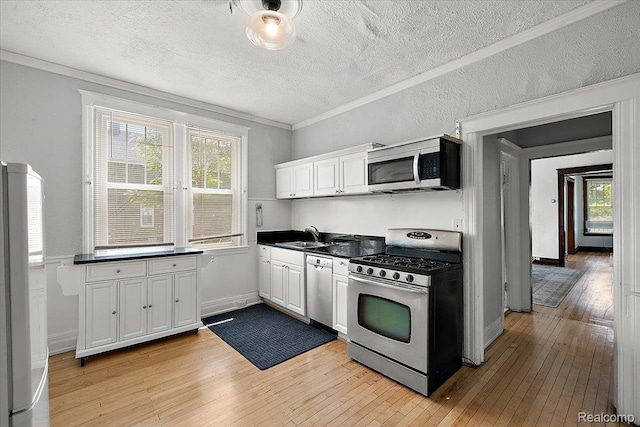 2160 Concord St, Detroit, MI 48207 - kitchen with stainless steel appliances, light wood-style flooring, ornamental molding, white cabinetry, and dark countertops