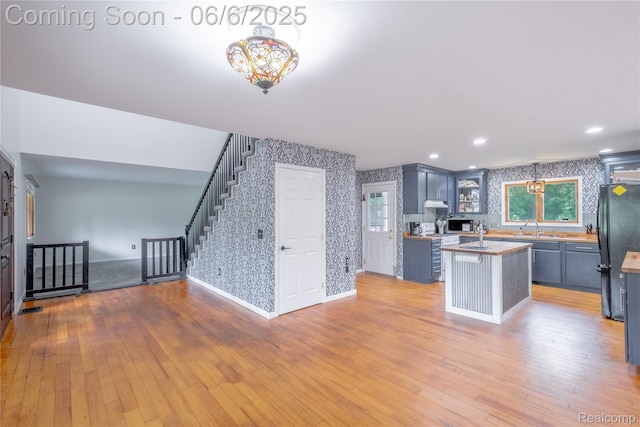 12631 9 Mile Rd, South Lyon, MI 48178 - kitchen with wallpapered walls, freestanding refrigerator, an island with sink, baseboards, and wood-type flooring