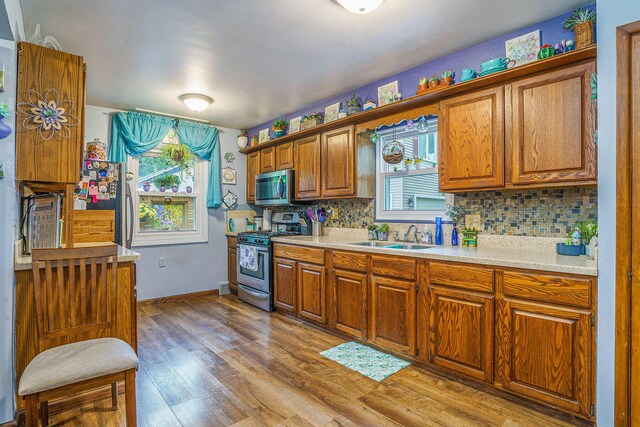 740 Halena St NE, Grand Rapids, MI 49505 - kitchen with appliances with stainless steel finishes, a sink, brown cabinets, light wood finished floors, and tasteful backsplash