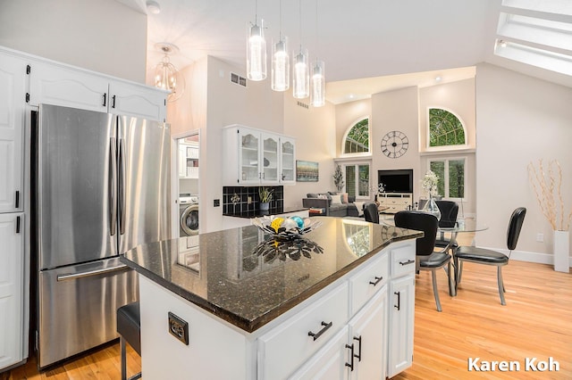 240 Pettis Ave NE, Ada, MI 49301 - kitchen with freestanding refrigerator, washer / dryer, a towering ceiling, light wood finished floors, and dark stone countertops
