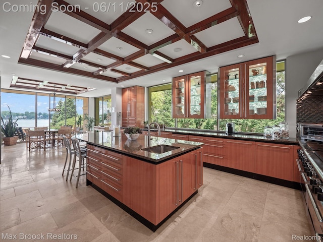 4790 Dow Ridge Rd, Orchard Lake, MI 48324 - kitchen featuring a sink, dark stone countertops, coffered ceiling, a kitchen island with sink, and brown cabinetry