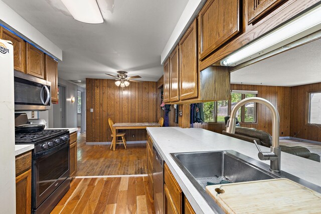 3618 Grape Ave NE, Grand Rapids, MI 49525 - kitchen featuring appliances with stainless steel finishes, a sink, wood walls, brown cabinets, and dark wood-style floors