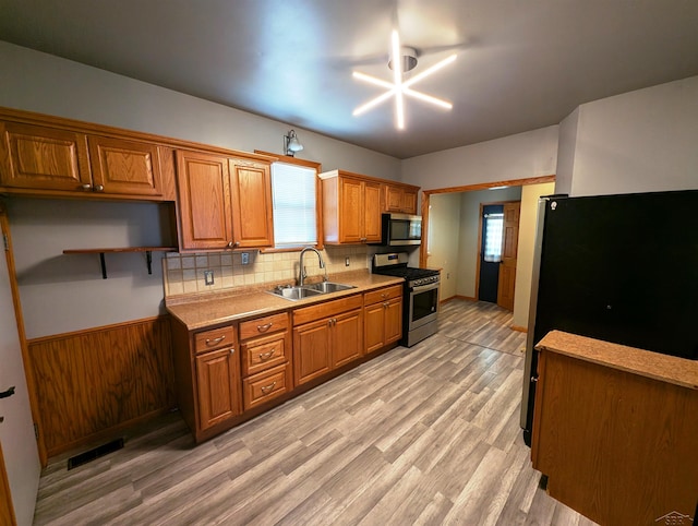 208 State St, Bay City, MI 48706 - kitchen with appliances with stainless steel finishes, a sink, brown cabinets, backsplash, and light wood-style floors