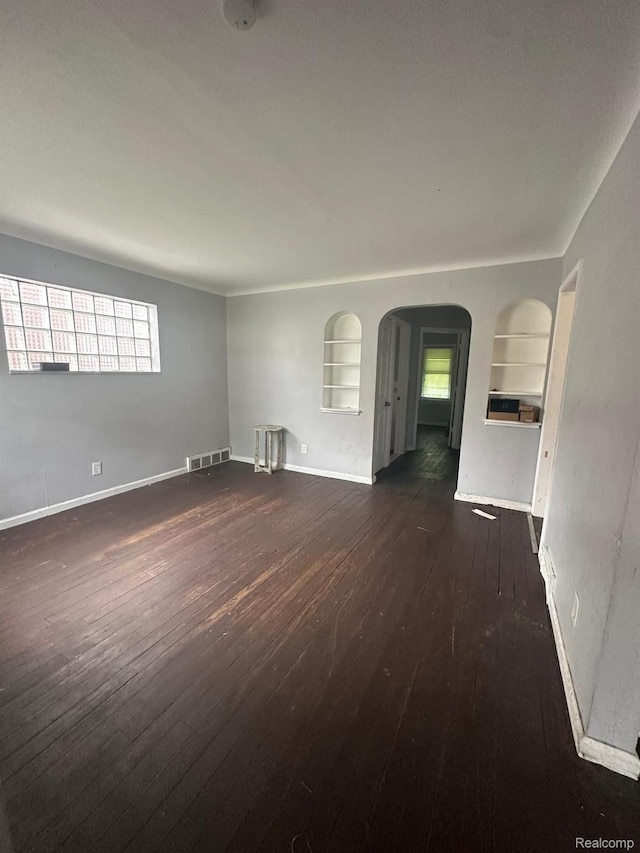 9317 Ward St, Detroit, MI 48228 - empty room featuring built in features, dark wood-style flooring, arched walkways, and plenty of natural light