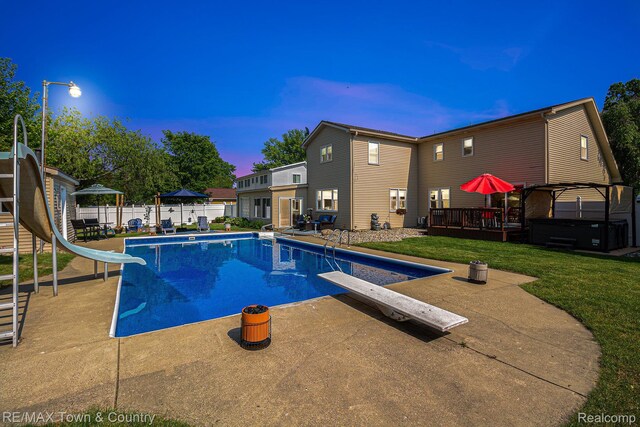 813 Birchwood Dr, Flushing, MI 48433 - pool at dusk featuring a diving board, a water slide, a covered hot tub, and a patio