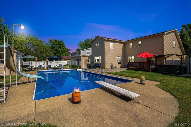 813 Birchwood Dr, Flushing, MI 48433 - pool at dusk featuring a covered hot tub, a diving board, a water slide, and a patio