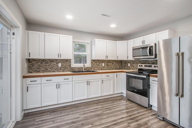 854 Upton Ave, Battle Creek, MI 49037 - kitchen featuring appliances with stainless steel finishes, a sink, butcher block countertops, decorative backsplash, and white cabinetry