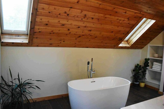 2735 Nestrom Rd, Muskegon, MI 49445 - bathroom featuring a skylight, a freestanding tub, wood finished floors, baseboards, and vaulted ceiling