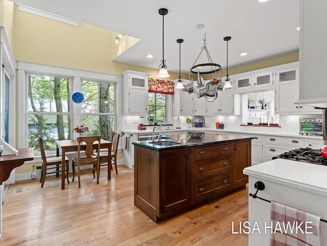 12857 Wilderness Trl, Grand Haven, MI 49417 - kitchen featuring a center island with sink, decorative backsplash, a sink, white cabinets, and glass insert cabinets