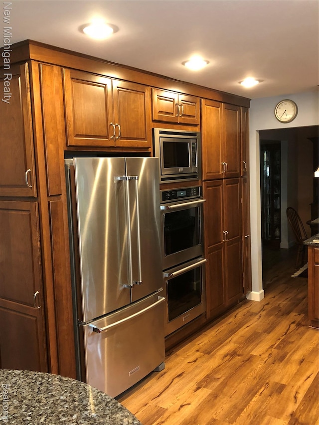 6567 Heaven Dr, Howell, MI 48855 - kitchen featuring appliances with stainless steel finishes, light wood finished floors, dark stone countertops, brown cabinets, and recessed lighting