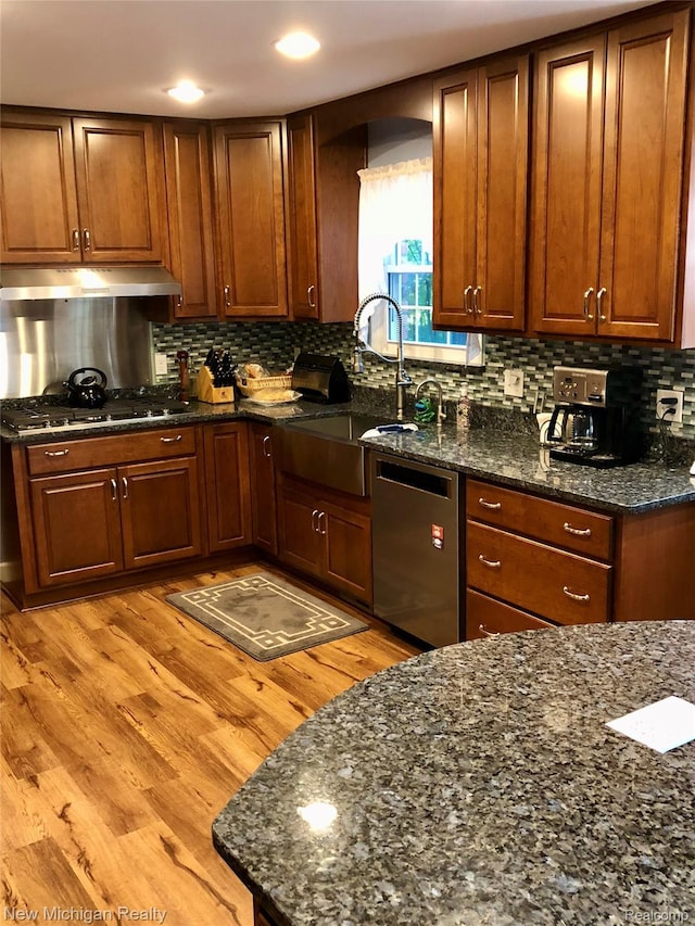 6567 Heaven Dr, Howell, MI 48855 - kitchen with stainless steel appliances, under cabinet range hood, decorative backsplash, dark stone counters, and light wood finished floors