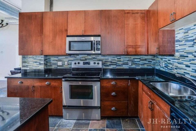 600 NW Broadway Ave Unit 318, Grand Rapids, MI 49504 - kitchen with stainless steel appliances, a sink, backsplash, dark stone counters, and brown cabinetry