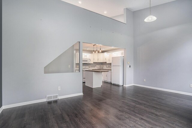 302 NE Xing, Holland, MI 49423 - unfurnished living room featuring dark wood-type flooring, baseboards, a towering ceiling, a chandelier, and recessed lighting