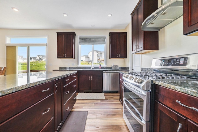 1162 Cooks Corner Ct SE, Byron Center, MI 49315 - kitchen with appliances with stainless steel finishes, wall chimney range hood, a sink, light wood-style flooring, and dark stone counters