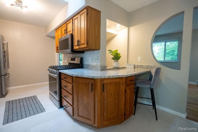 24449 Laurel St, Flat Rock, MI 48134 - kitchen featuring appliances with stainless steel finishes, brown cabinets, light stone counters, arched walkways, and baseboards