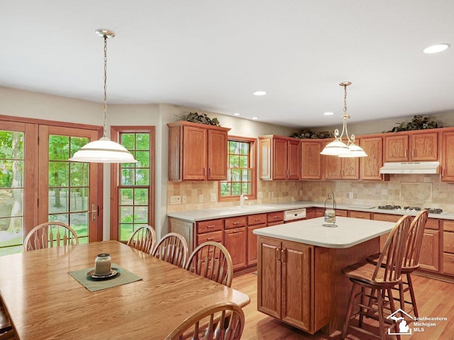 9241 Legacy Ct, Temperance, MI 48182 - kitchen with under cabinet range hood, light wood finished floors, a kitchen island, light countertops, and a kitchen bar